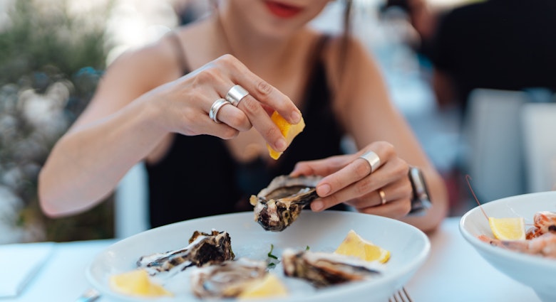 Woman squeezes lemon on to oysters while dining alone